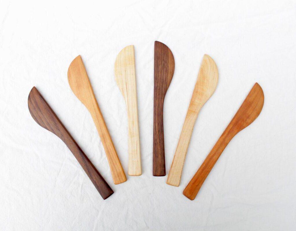 Top-down view of five butter, cheese or soap-beveling knives. They are arrayed in an arc, showing off the contrasting colors of the cherry, walnut and maply hardwoods. Each one is handmade and unique, but the overall shape is the same.