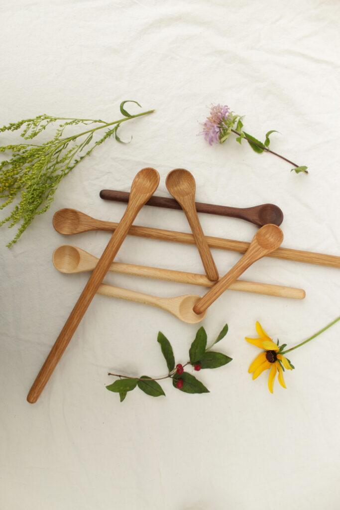 Stirring spoons, cooking spoons, salt spoons, mixing spoons... all different spoons are strewn about on a table amongst some flowers. Each spoon was handcrafted with care in the Rondout Valley