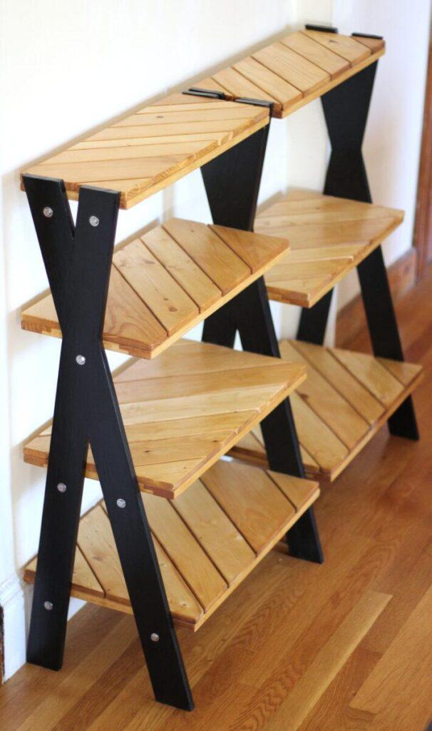 Two handmade, custom pantry shelves stand side by side on a wood floor with a white background. The shelves have diagonal pine shelves and a black X for legs. The shelf on the left has four shelves, and the on on the right has three shelves. Despite the modern look, they are made from salvaged construction scraps.