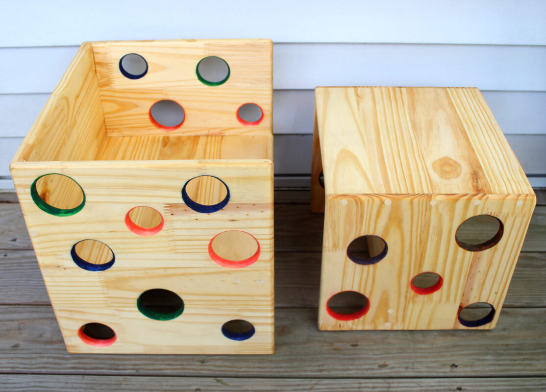 child's cube chair and desk made of deconstructed furniture Cube chair and matching desk with colorful holes: red, blue and green. Set on one side, these are chairs for children. Set on the other, they are desks for children. The smaller one fits inside the larger one when turned the right way. They are made of salvaged/upcycled wood in the Hudson valley by an intependent maker/artisan. They sit on a wooden porch.