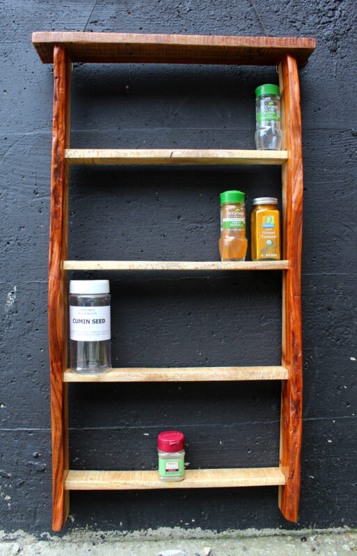 hanging spice rack made from discarded pallets Hanging spice rack made from upcycled and reclaimed pallets. It has four shelves containing a few different herbs. Behind the shelf is a black cement wall. Made by Hudson Valley woodworker, Flotsam Made.