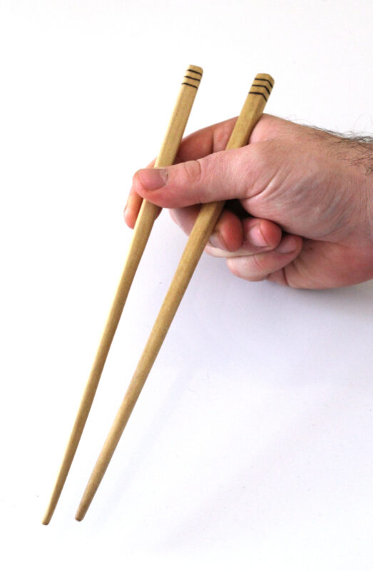 chopsticks made from Tulip Poplar scraps Handmade chopsticks made from reclaimed tulip poplar. The top of the chopsticks have three dark lines etched around them. A hand holds them over a white backgrount. Sustainable kitchenware designed and made near Ellenville New York.